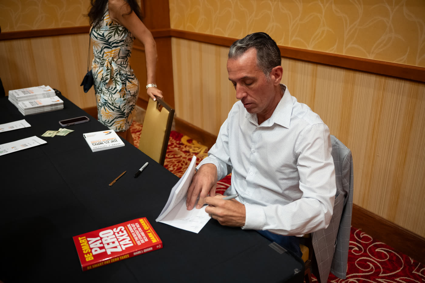 Mark Quann signing books at Elevate 2026, with Be Smart Pay Zero Taxes on the table